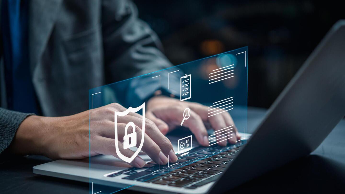 A man in a suit types on a laptop, with a transparent graphic overlay of cybersecurity icons, such as a shield with a lock.