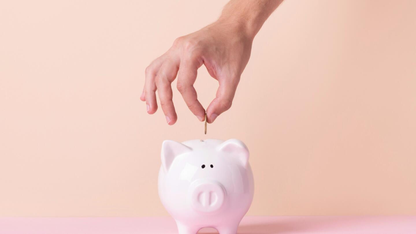Eine Hand wirft eine Münze in ein rosa Sparschwein. Das Bild symbolisiert, wie eine frühzeitige Event-Budgetplanung in Q4 hilft, Kosten zu sparen.