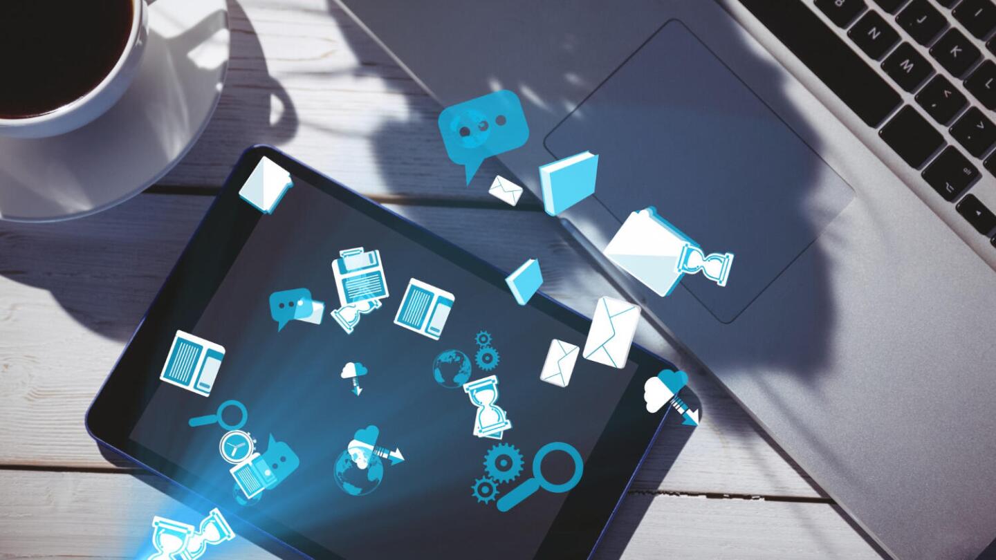 table with laptop, ipad and coffee with bright blue icons floating around that suggests digital communication
