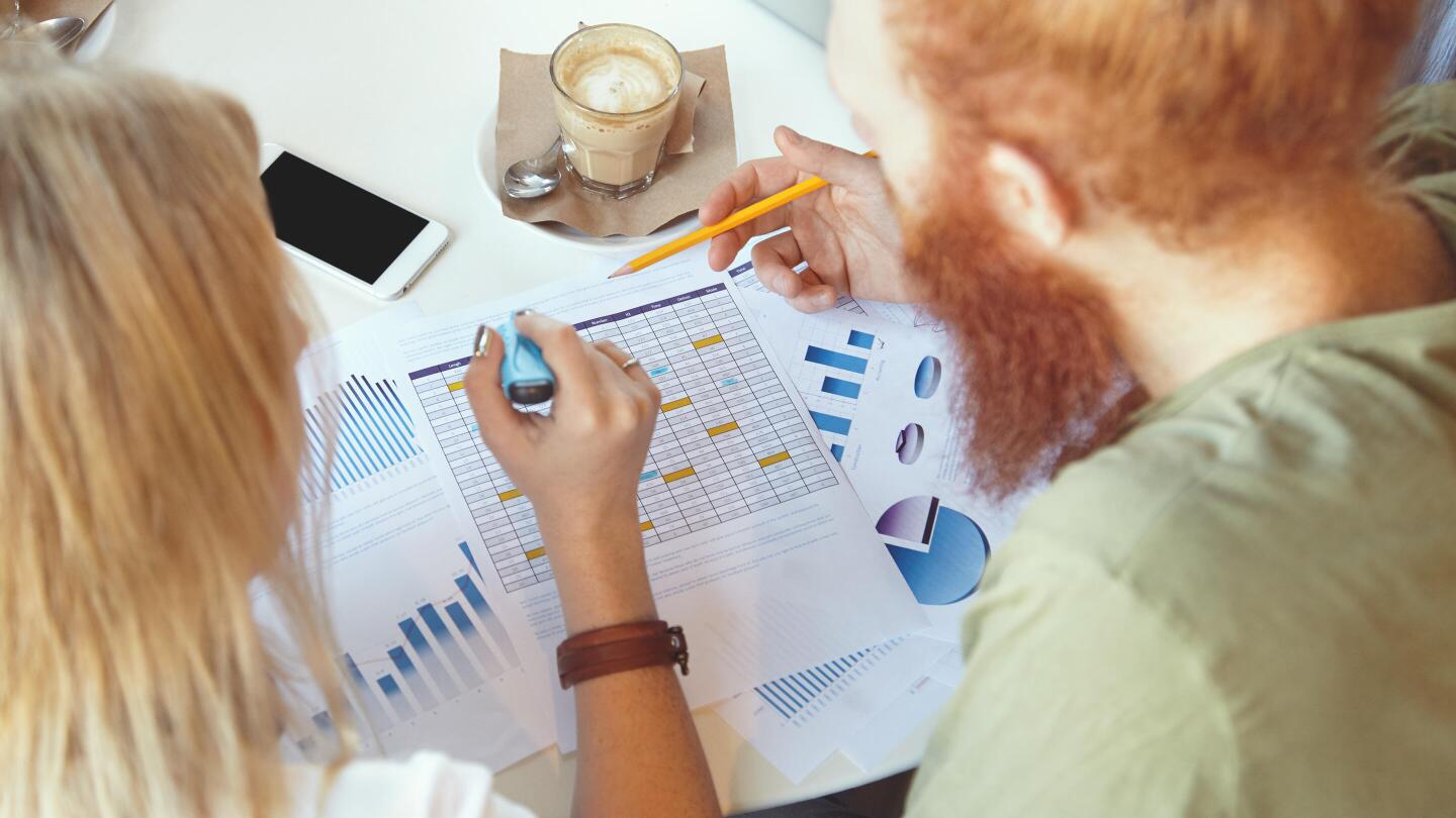 Two people are sitting at a desk and analyzing printed charts and spreadsheets together.