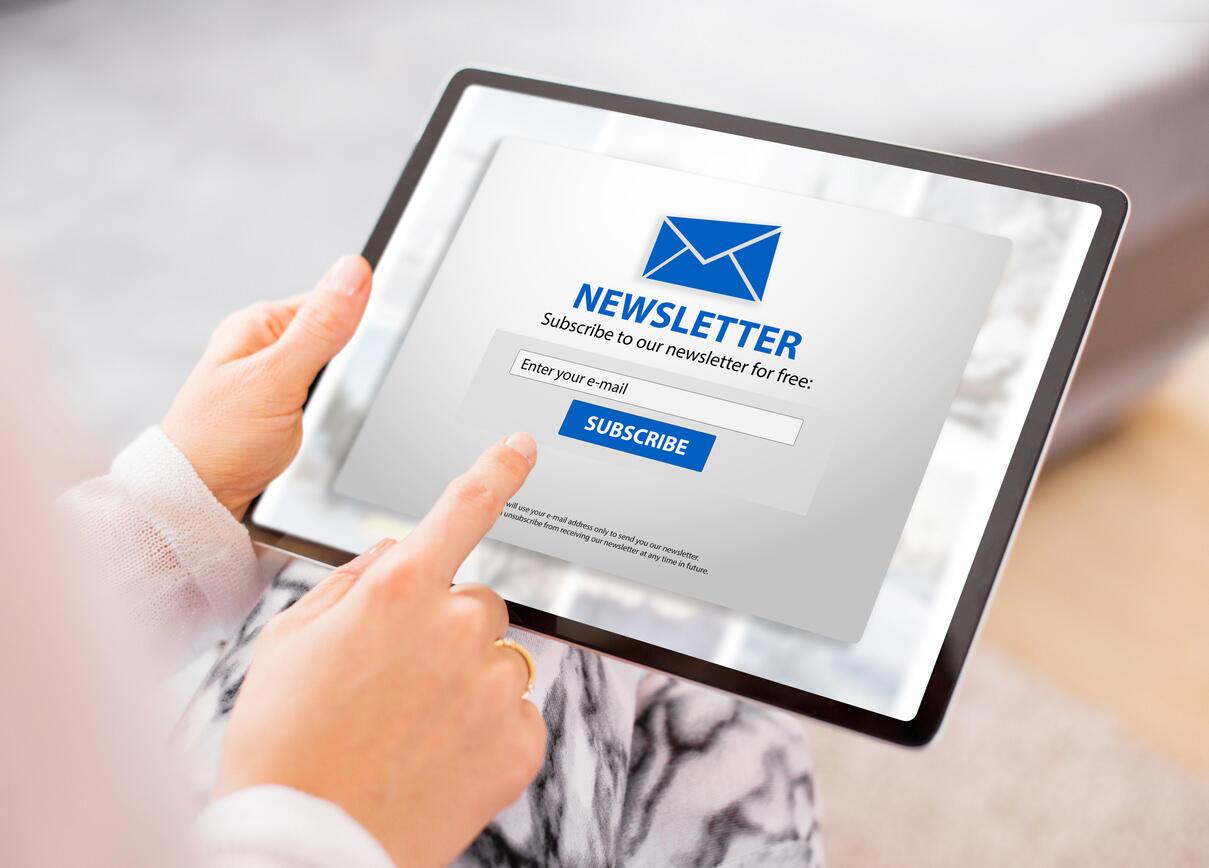Person hält ein Tablet und tippt auf ein Newsletter-Anmeldeformular mit der Aufforderung, die E-Mail-Adresse einzugeben und auf ‚Subscribe‘ zu klicken.
